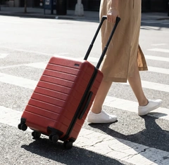 A red ribbed suitcase rolling through a sunlit city street